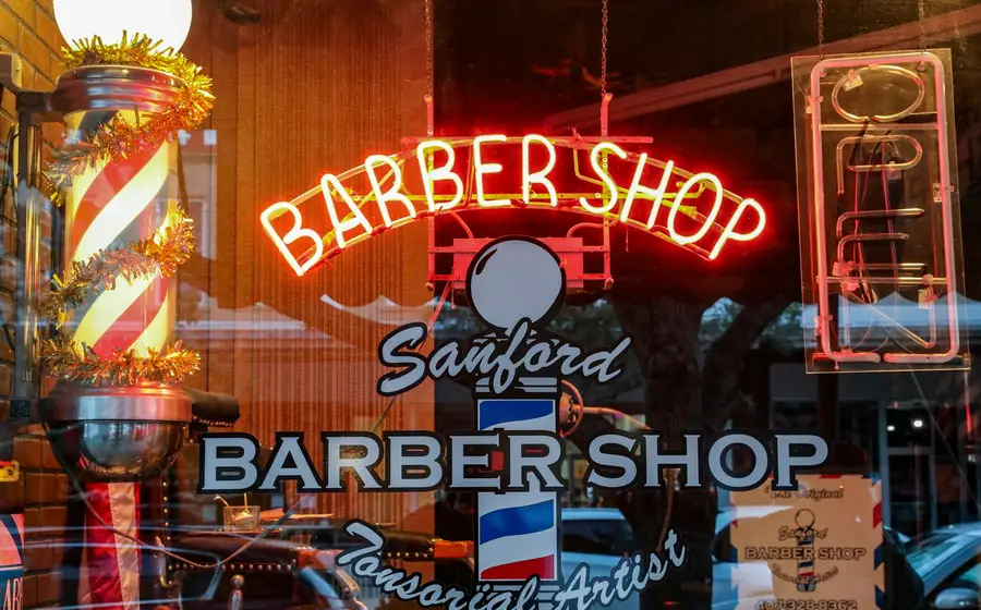A barber shop window lit by neon signs at night